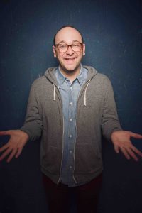 Comedian Josh Gondelman standing and holding his hands out