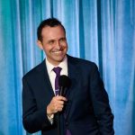 Clean comedian Tony Deyo on stage, wearing a suit and holding a microphone